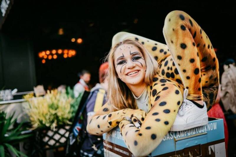 Young woman in cheetah costume smiling, sitting in a box at an event.