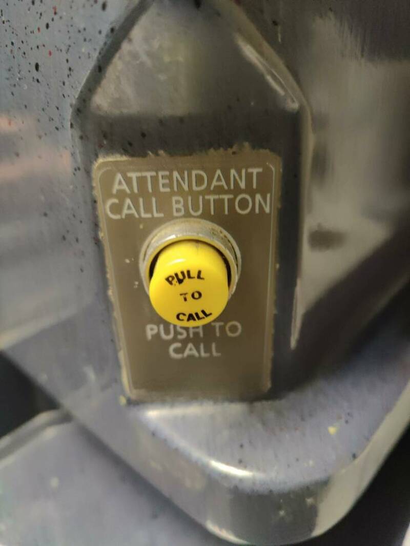 Attention call button with a yellow pull to call label on a metallic surface.