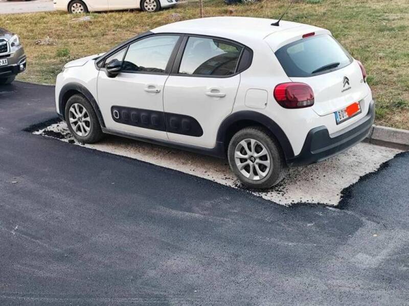 White Citroën car parked on a patch of gravel on the side of the road.