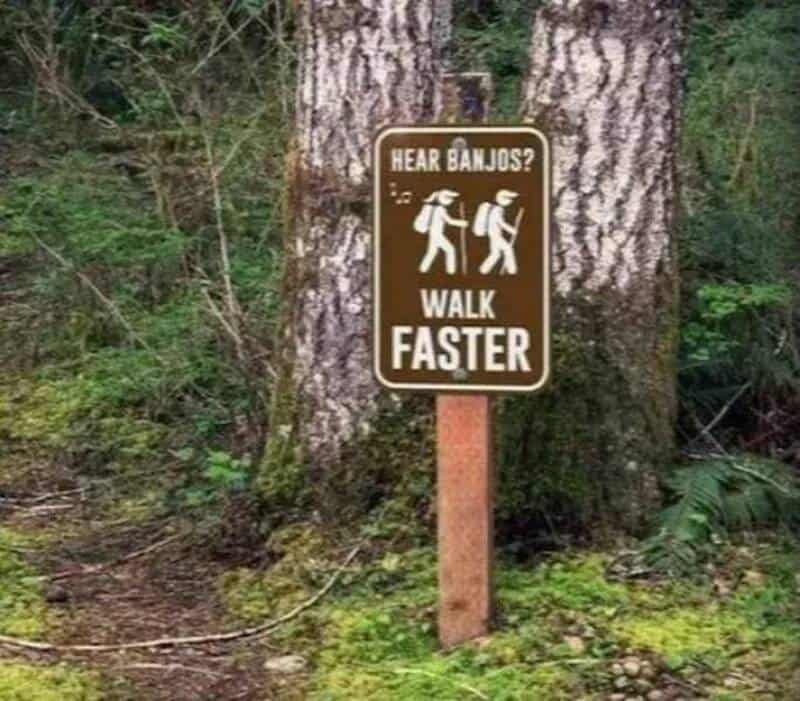 Sign on tree says 'Hear Banjos? Walk Faster' with images of two people walking.