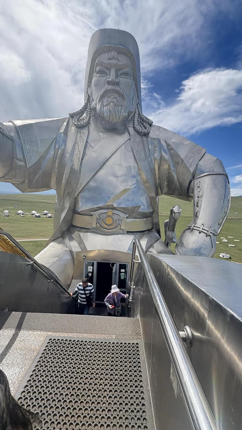 Large metallic statue of a warrior with a beard and armor, under a partly cloudy sky.