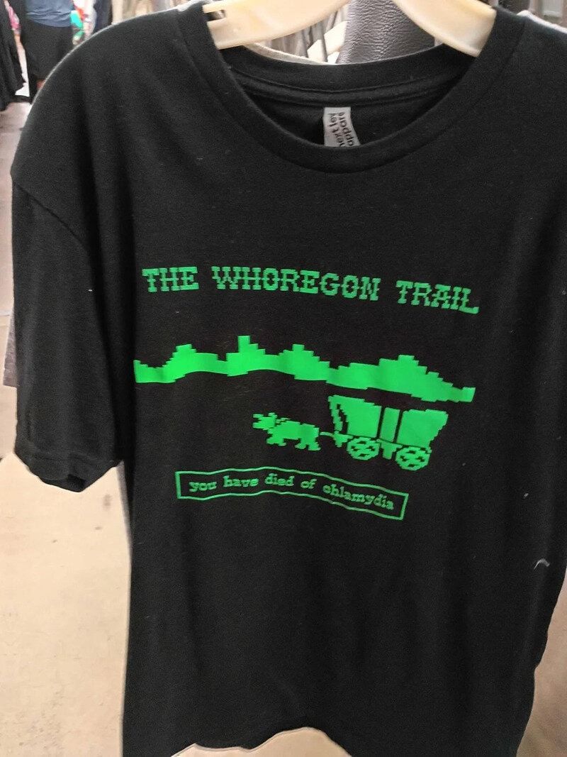 Black T-shirt with green pixel art of a trail and text about the 'The Whoregown Trail'.
