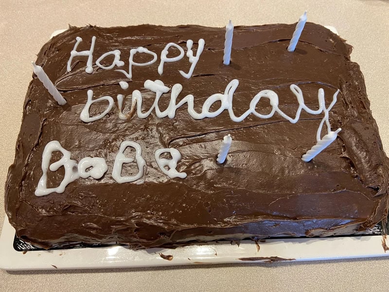 Chocolate birthday cake with white icing writing and blue candles, 'Happy birthday BoBe'.
