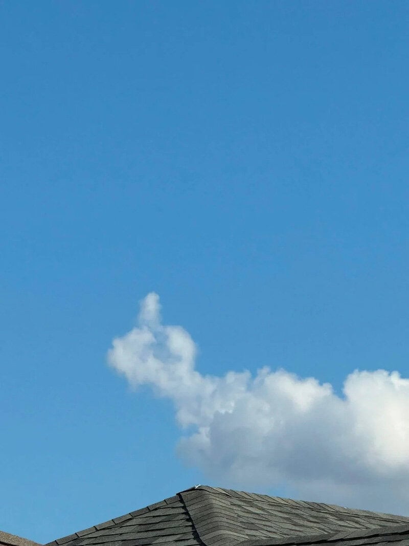 Blue sky with a small cloud above a house roof.