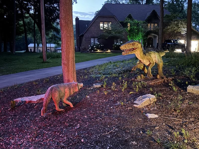 A dinosaur and a dog in a yard at night, with a house in the background.