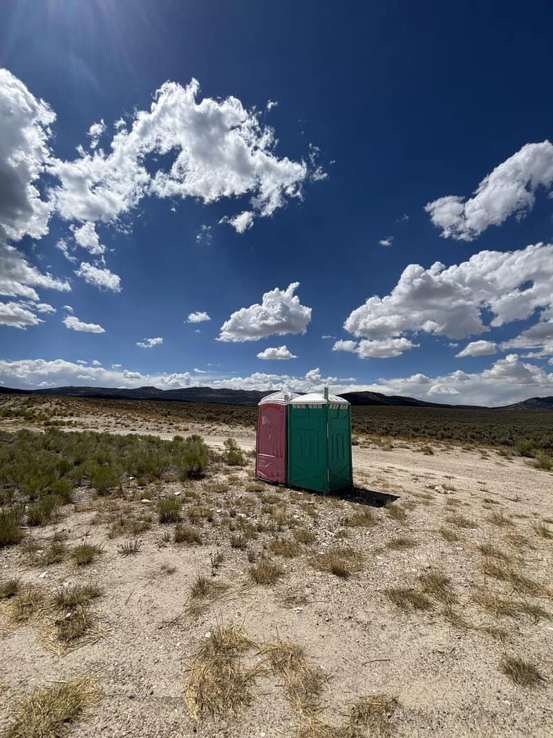 Two portable toilets in a desert landscape under a blue sky with clouds.