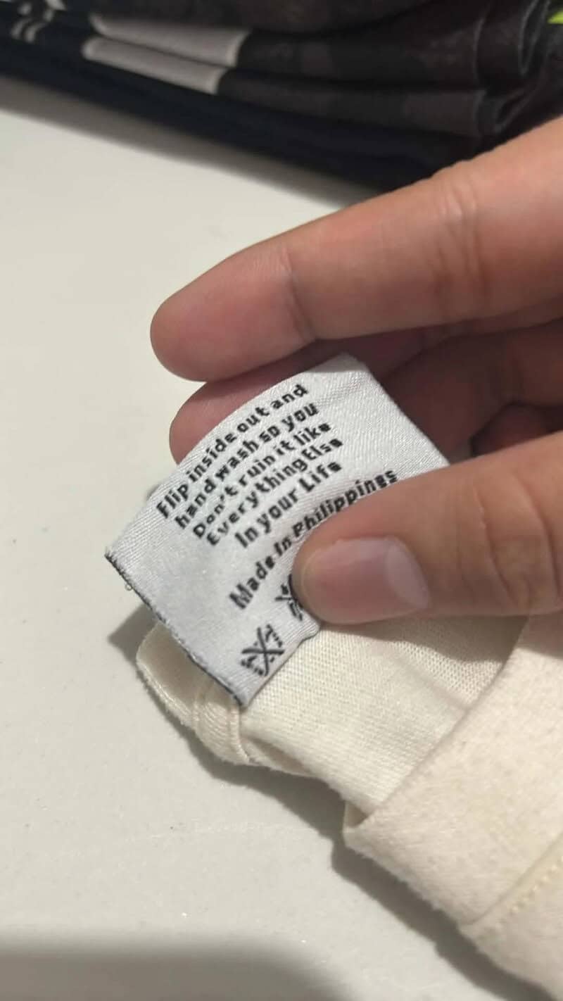 Clothing label with washing instructions, held by a person's hand.