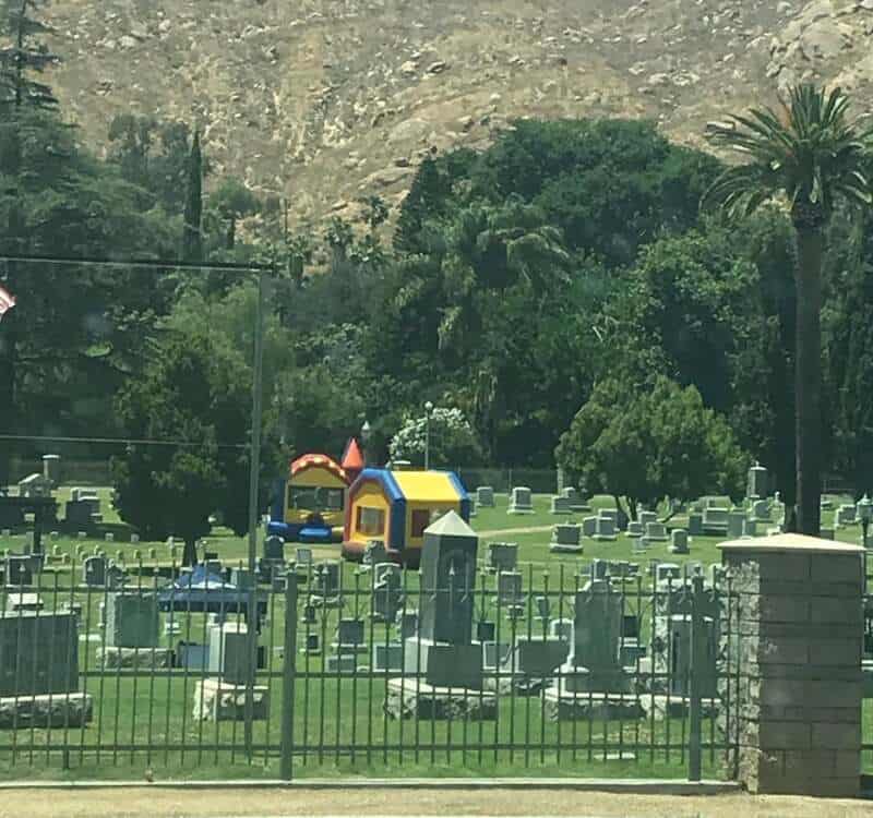 Colorful inflatable bounce houses in a cemetery with gravestones and trees.