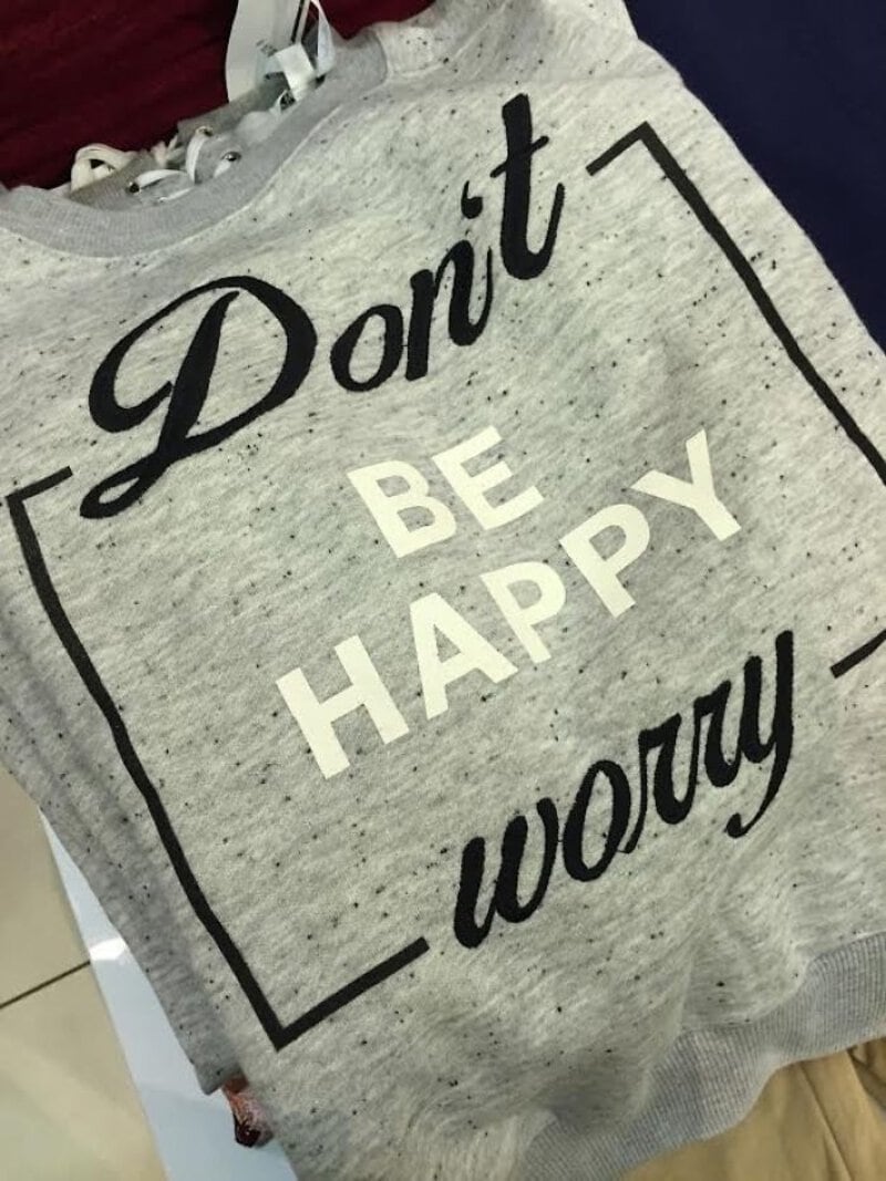 Gray sweatshirt with the text "Don't BE HAPPY worry" in black and white letters.