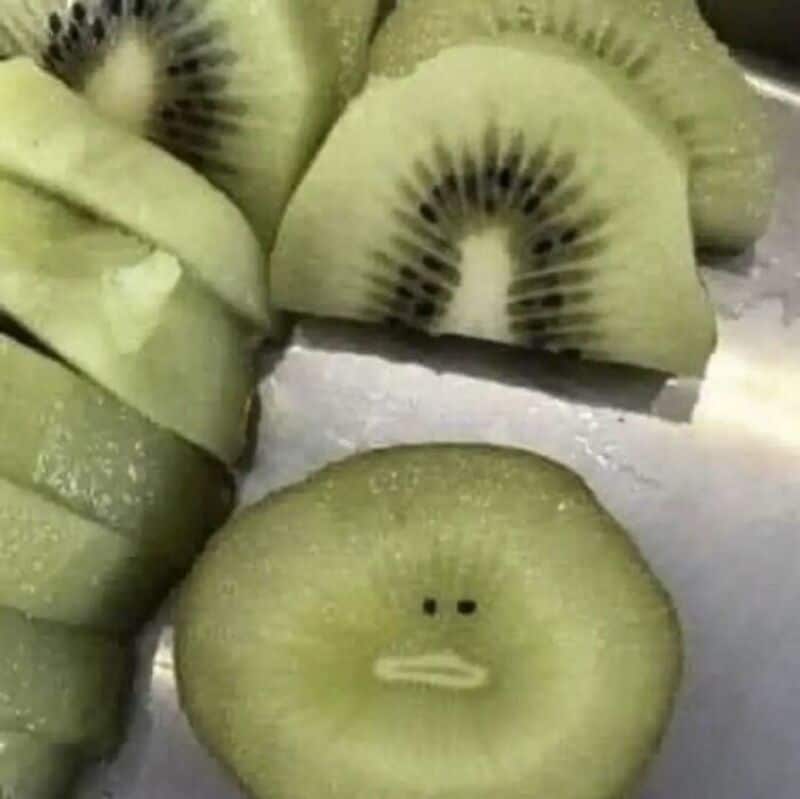 Kiwi slices with a face drawn on one slice, resembling a face with a neutral expression.