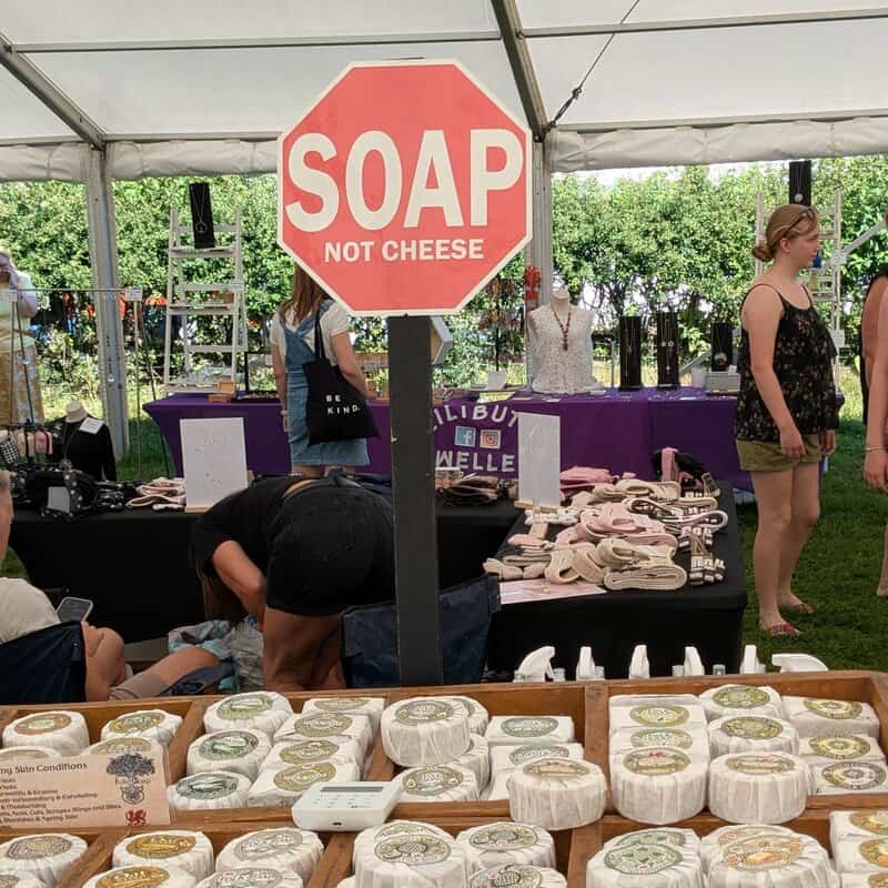 Sign reads 'SOAP NOT CHEESE' at a market stall with soap and other items displayed.