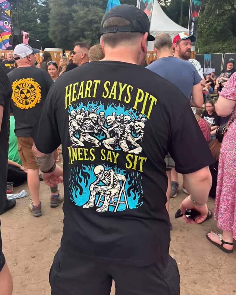 Man wearing black T-shirt with skeletons and humorous text at outdoor event.