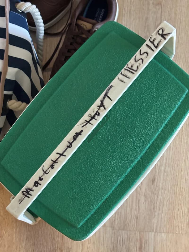 Green plastic container with a wooden stick labeled 'MORCANT LA TAT MESSIER' on top.