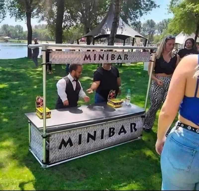 Miniature bar stand with 'MINIBAR' sign, set outdoors near a lake.