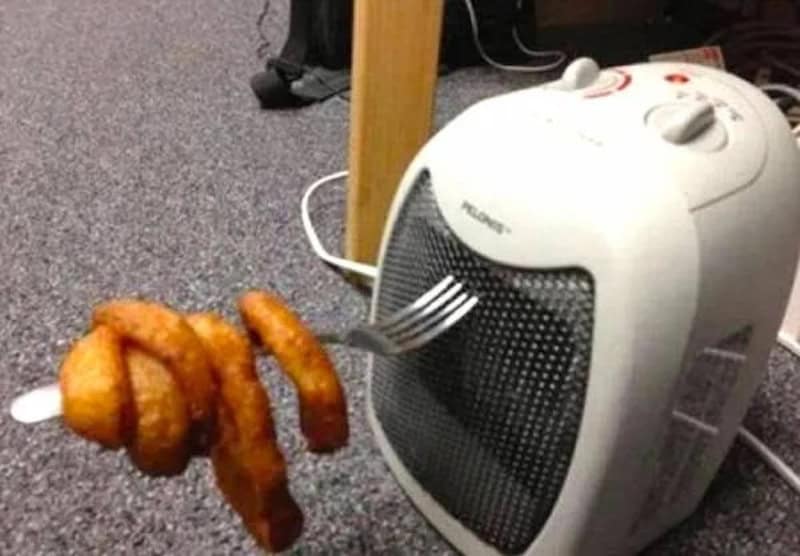 Fried onion rings hanging from a fork near a space heater.
