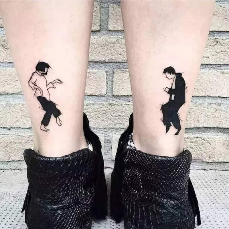 Two tattoos of dancing figures on person's calves, with black boots.