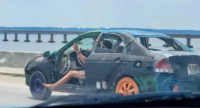Person with legs out of a black car on a bridge, holding a phone.