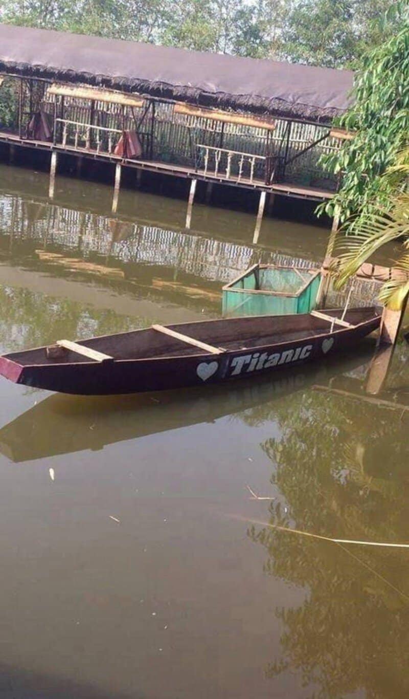 A boat named 'Titanic' floating in a river with a dock and hut in background.