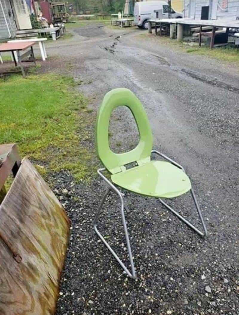 Green chair with a backrest shaped like a toilet seat on a gravel path.