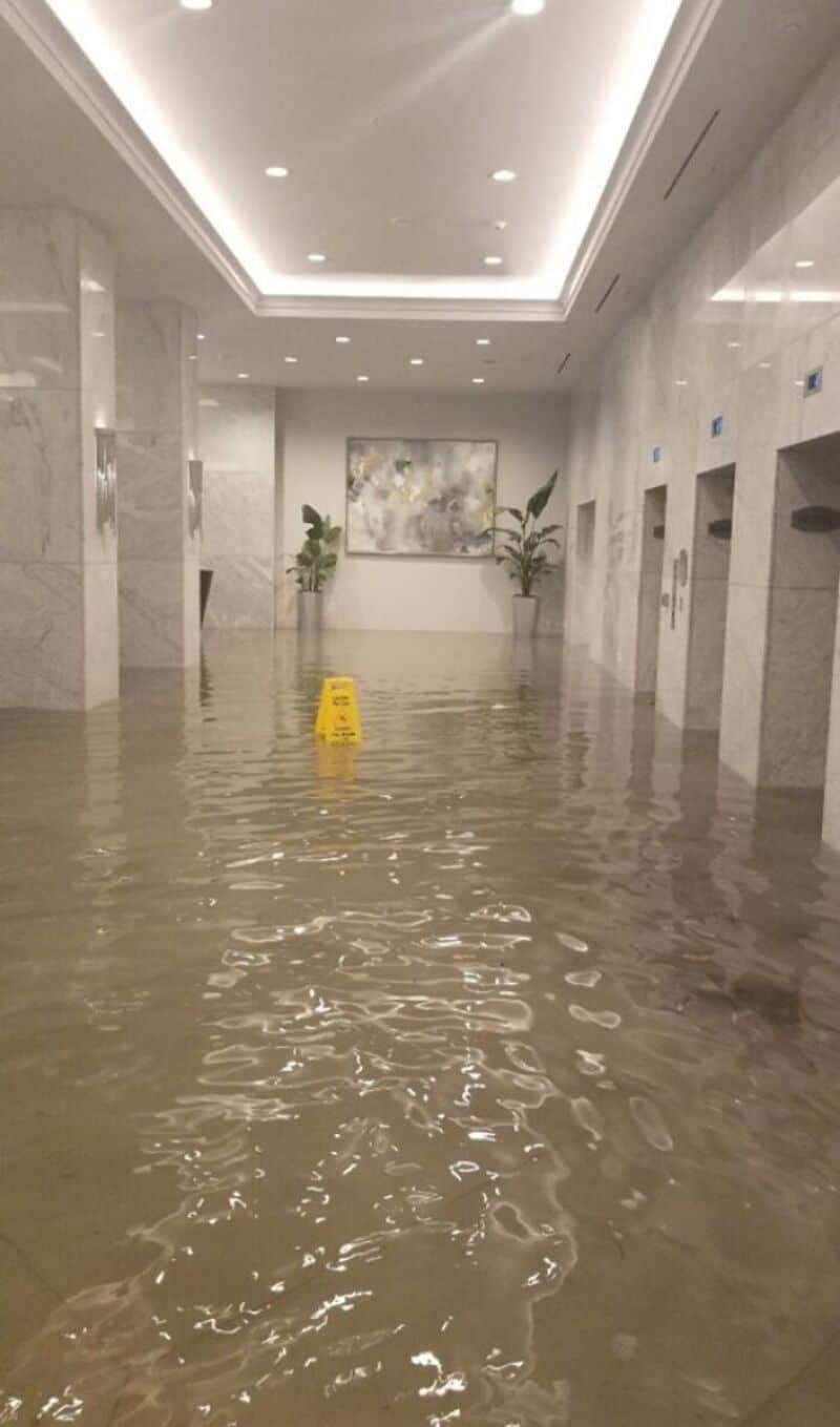 Flooded lobby with water reaching halfway up the floor, yellow caution sign in the center.