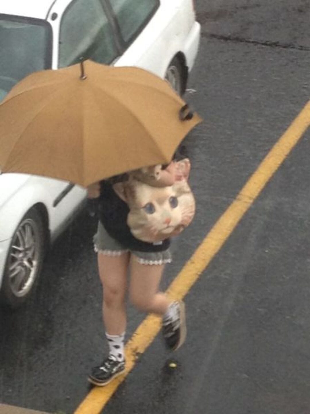 Person holding a large bag with a cat face print, under a yellow umbrella.