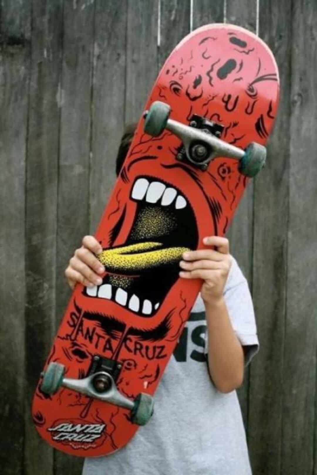 Person holding skateboard with a face design, covering their face.