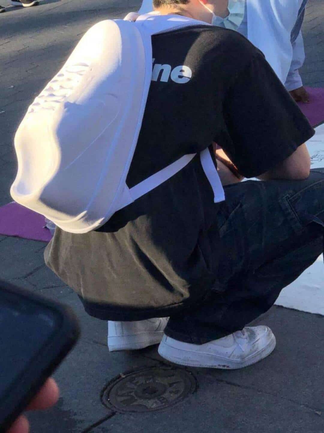 Person squatting on the street with a backpack and white sneakers.