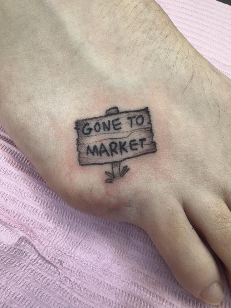 Tattoo of a sign saying 'GONE TO MARKET' on hand.