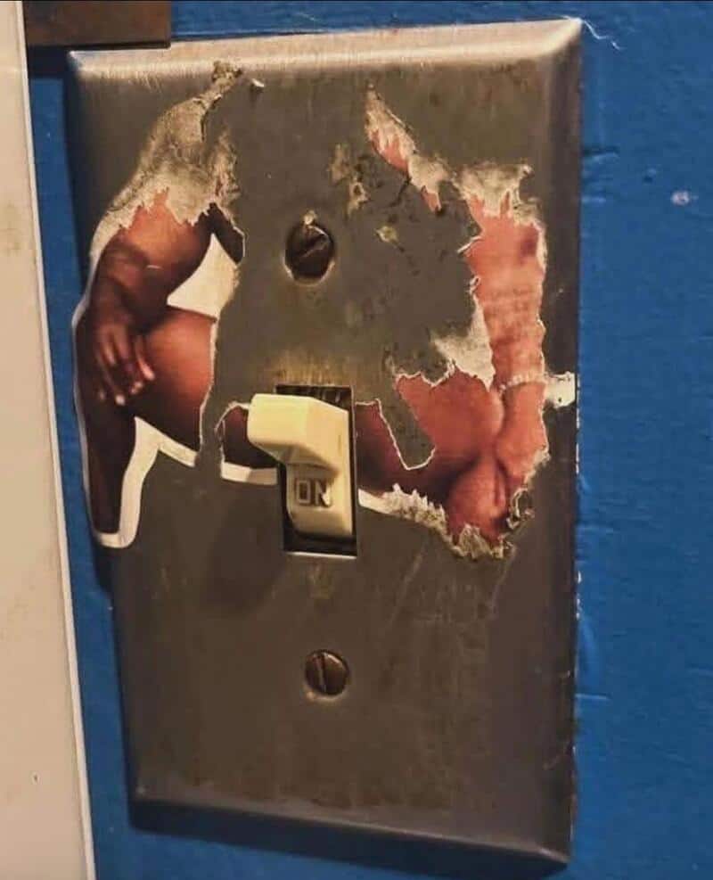 Torn wall plate cover with a hand and a foot visible behind it.