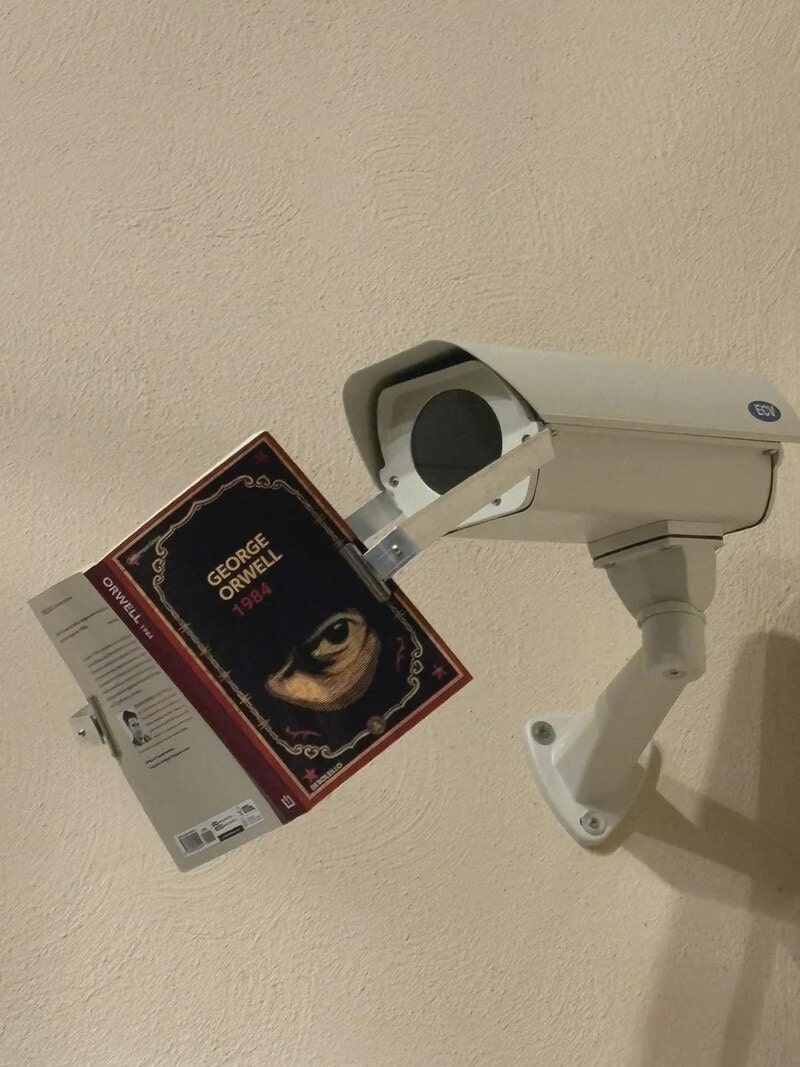 CCTV camera with a book titled 'George Orwell 1984' hanging from it.