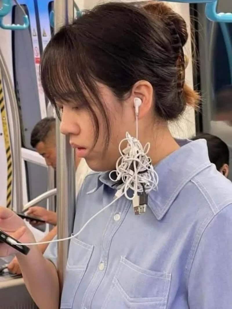 Young woman with tangled earphones on her neck, looking at her phone on a train.