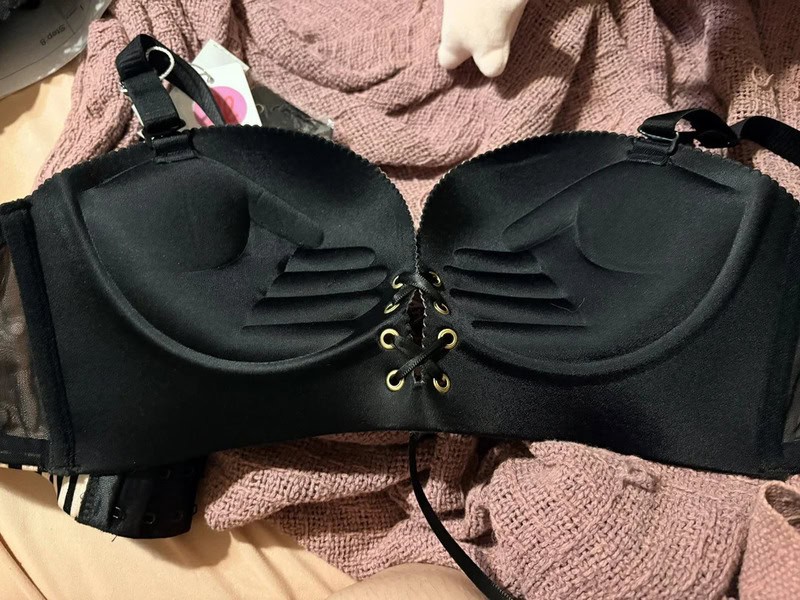 Black bra with lace-up front and padded cups on a pink blanket.