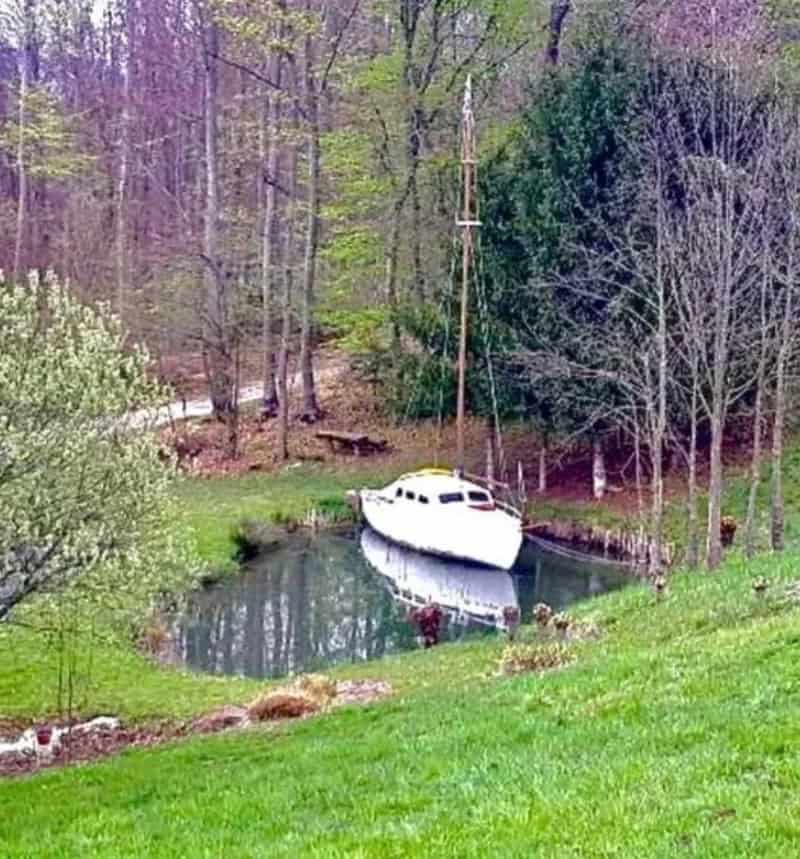 A boat is stuck in a small pond surrounded by trees and grass.