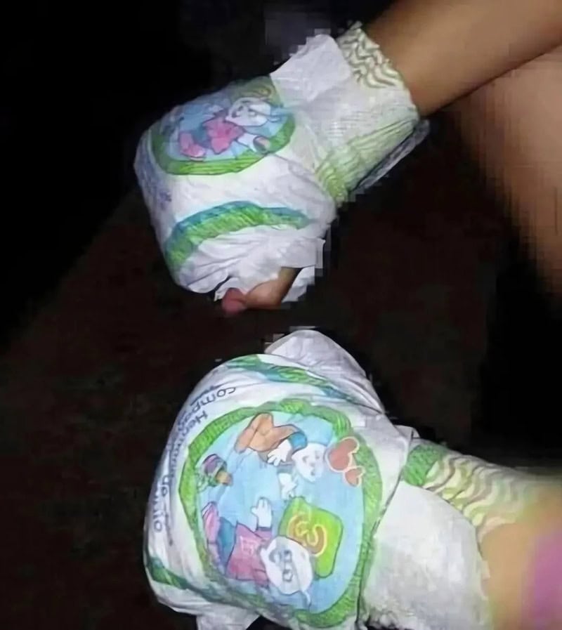 Child wearing diaper with cartoon characters, lying on dark surface.