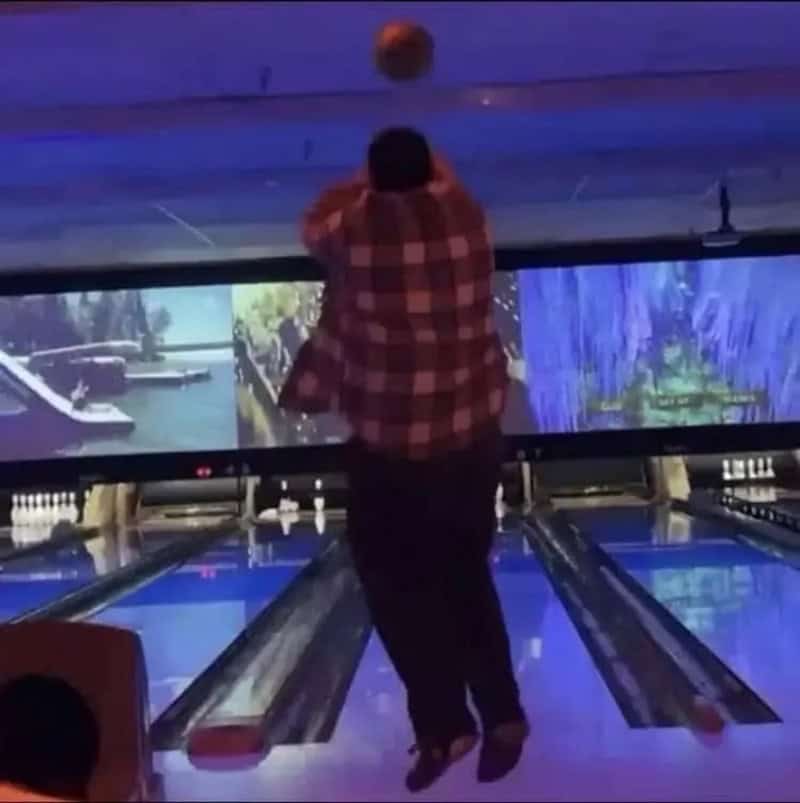 Person in plaid shirt bowling, ball mid-air, at a bowling alley.