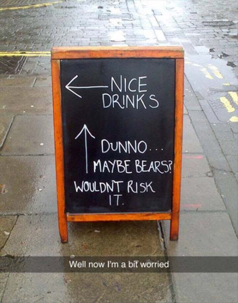Chalkboard sign with humorous message about drinks and bears, on a sidewalk.
