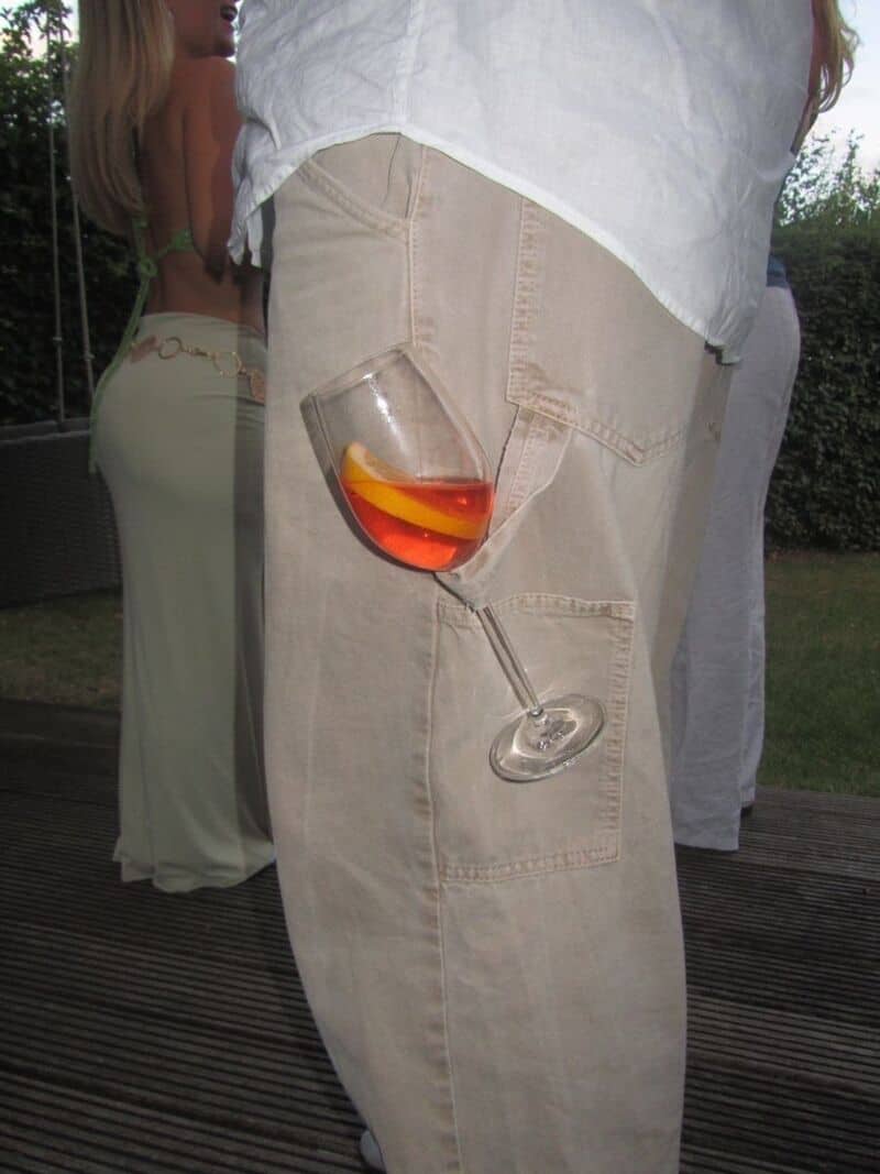 Glass of red wine in a person's pocket with a second glass on the ground.