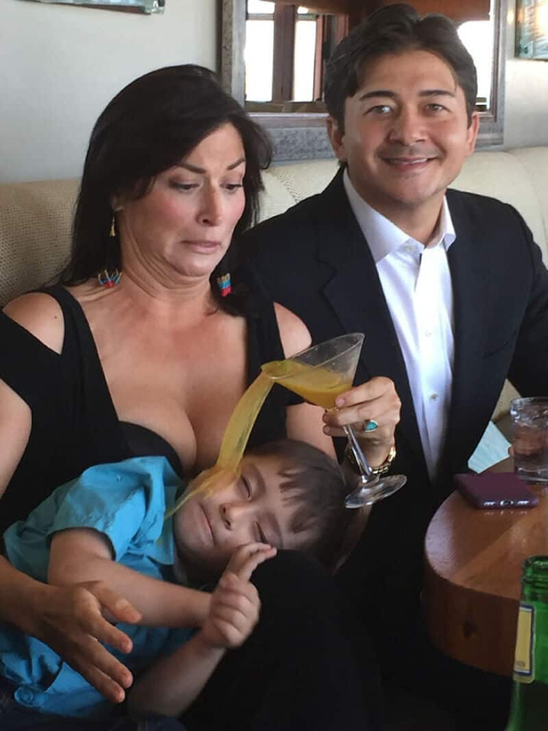 Family at a restaurant, woman with a drink, child resting on her lap, man smiling.