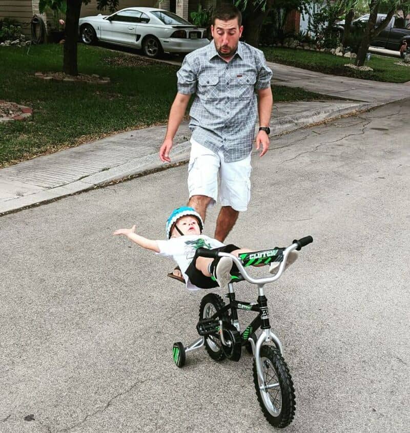 Man chasing a young girl on a bike in a park.