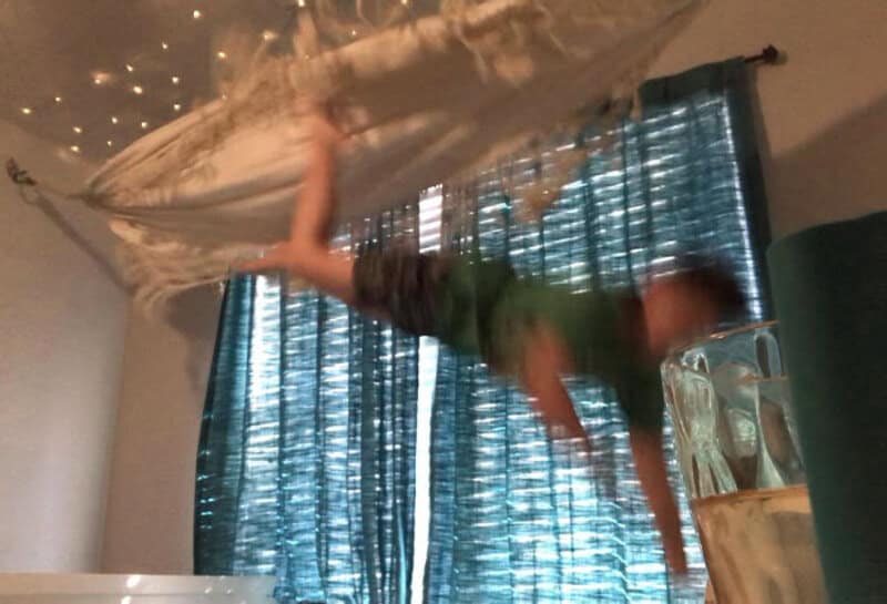 Child falling from bed onto a glass table, curtains and fairy lights in background.