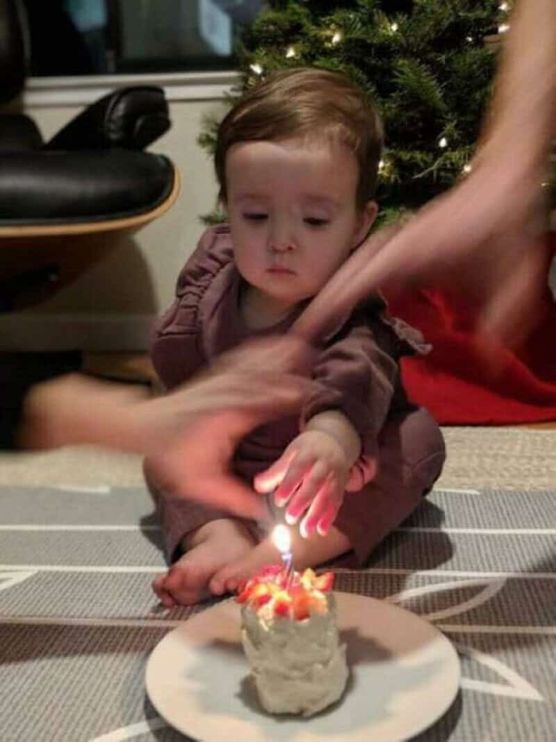 Child trying to blow out birthday candle with help from adults.