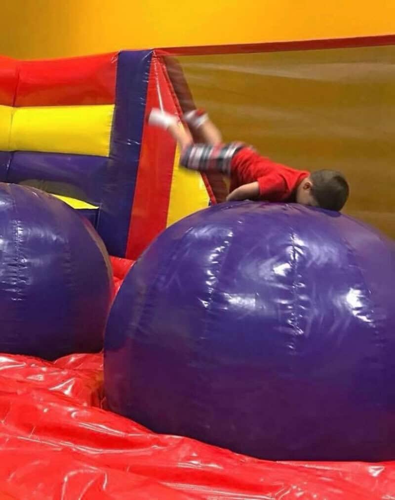 Child falling on large blue inflatable balls at indoor play area.