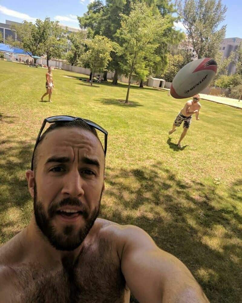 Man taking selfie with two kids playing with a rugby ball in park.