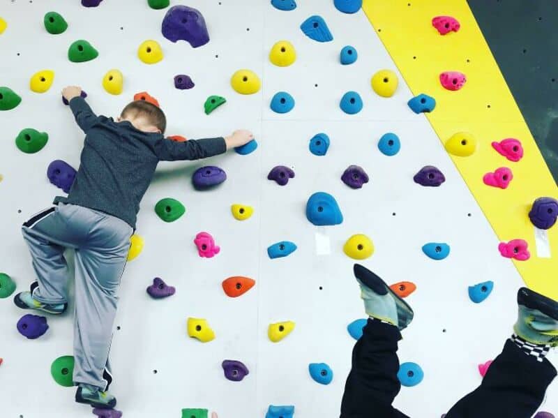 Child climbing colorful indoor rock wall with various holds.