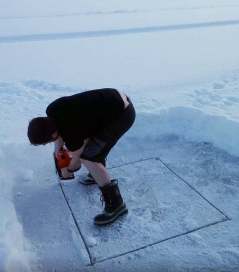 Person drilling ice within a marked square on snow.