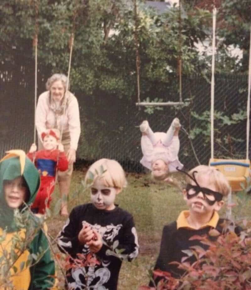 Children in costumes playing outside with an adult in the background.