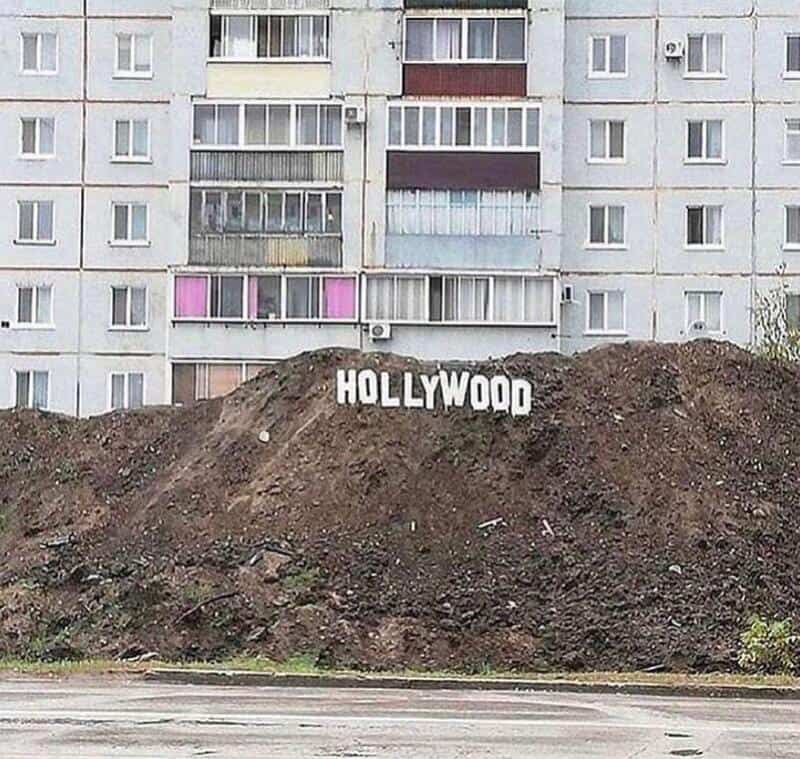 Hollywood sign on a dirt mound in front of an apartment building.