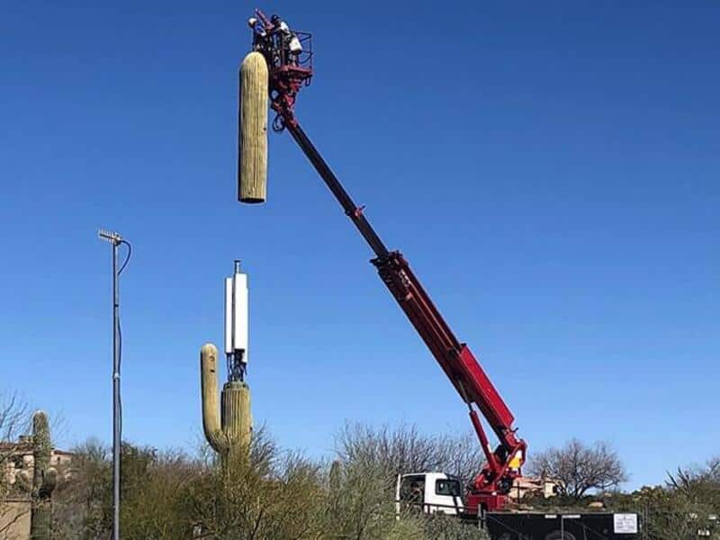 Worker in bucket lift installing a utility pole against a clear blue sky.
