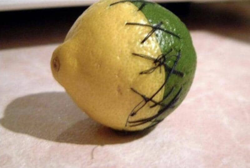 Lemon painted half yellow and half green with black stitches on the green side.
