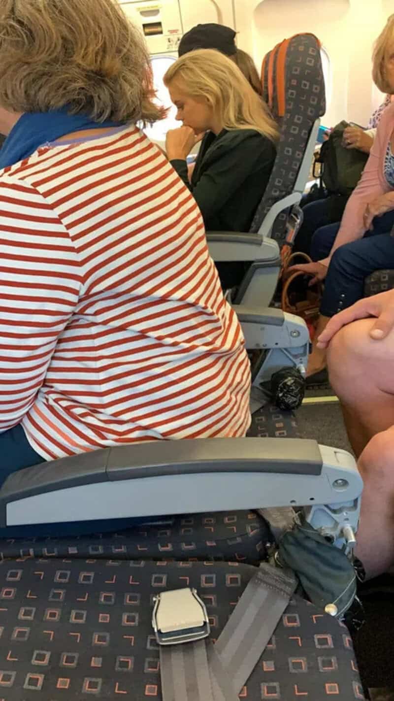 Passengers seated on an airplane, including a woman in a red and white striped shirt and a girl with.
